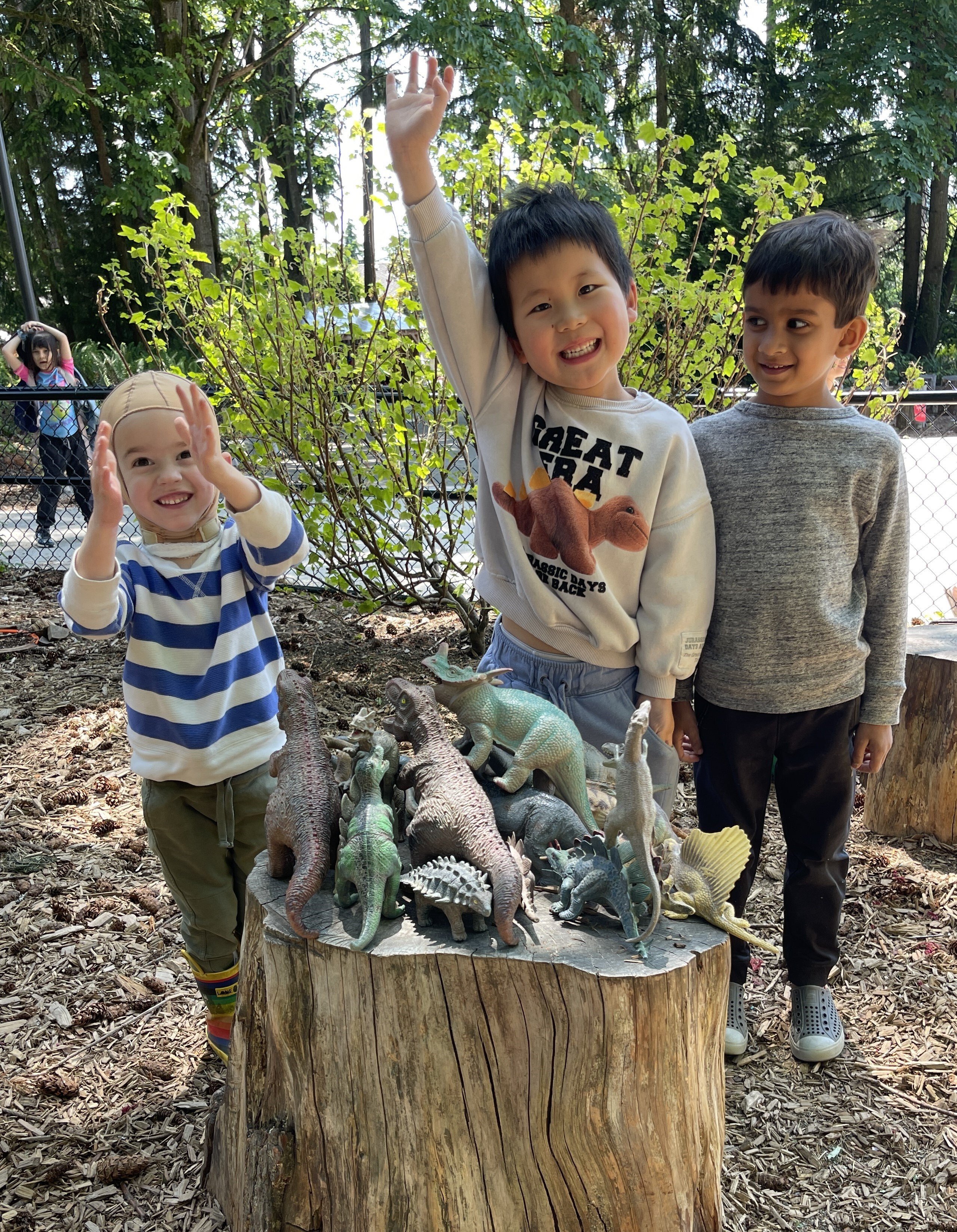 Three students plaing with model dinosaurs on a wooden stump