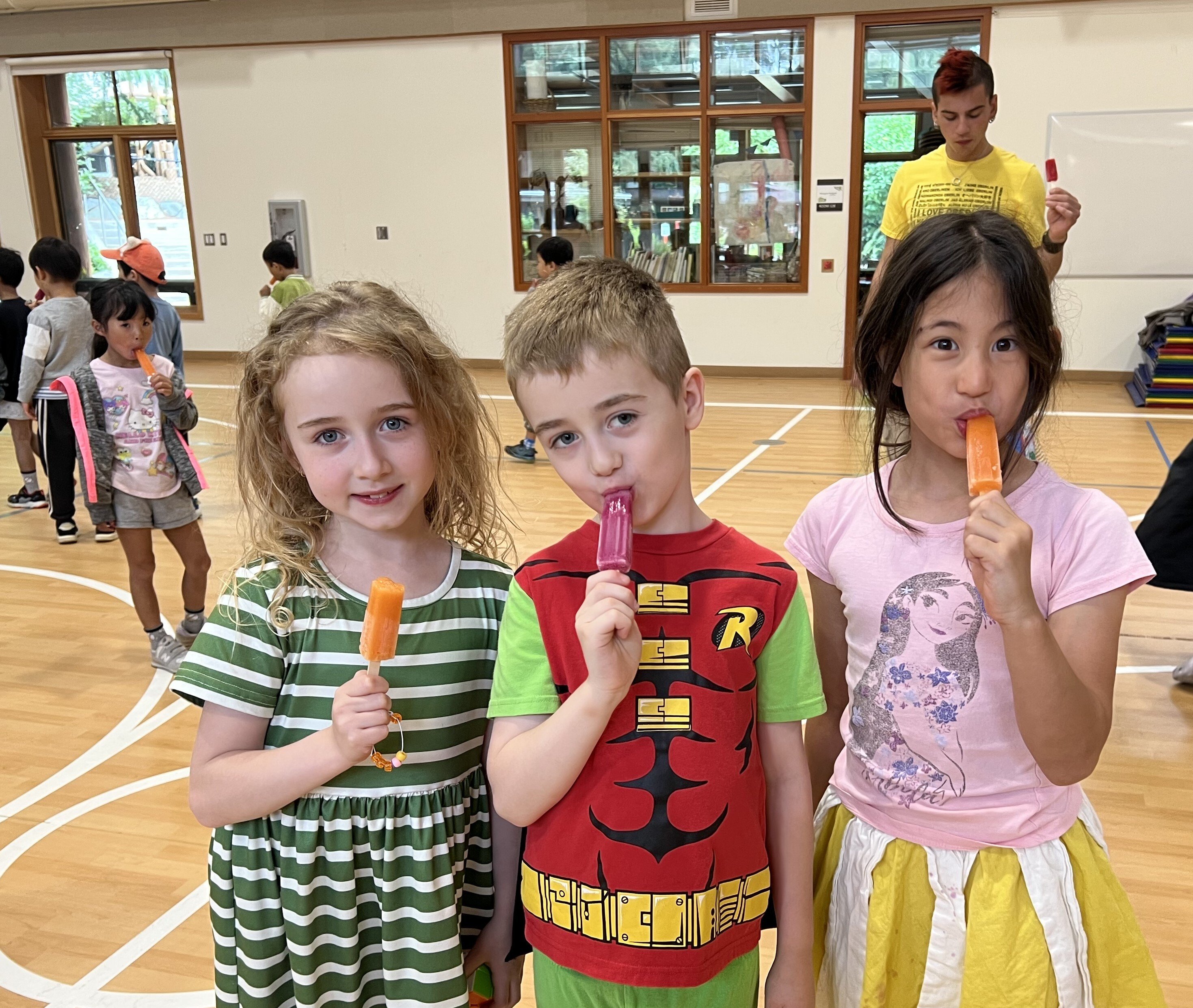 Three students with flavored popsicles in a gym