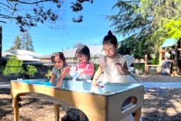 Three young children playing together at an outdoor sensory table